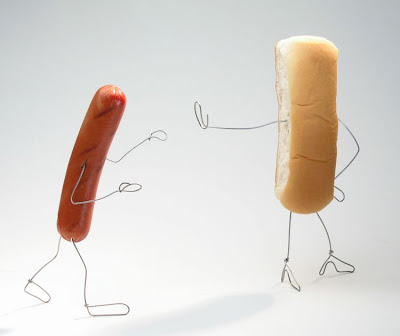 A hotdog and a hotdog bun, both with arms and legs made out of thing wire that's a little thinner than a paperclip. The hotdog has its arms in a gesture of pleading. The bun is turned away from the hotdog with its arm and hand extended in a stop gesture and a general I don't want to hear it vibe