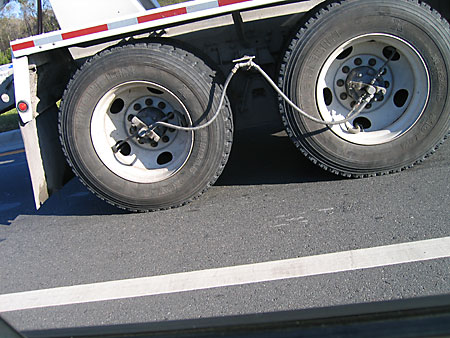 A photo of two back wheels of an eighteen wheeler with a small tube running between them that I think is for adjusting pressure on of the tires.