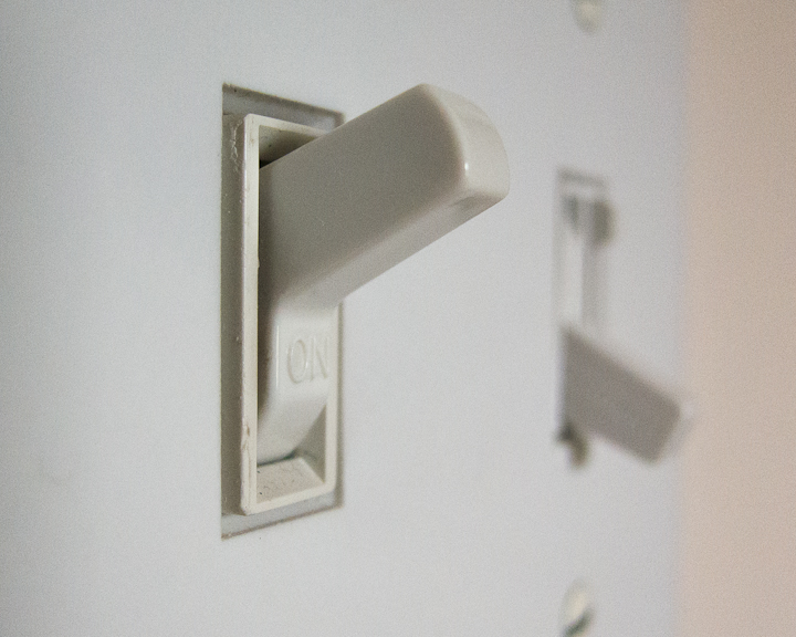 A close-up photo of a dual set of wall light switches. The light switch closest to the frame is flipped up with the word 'ON' visible on the bottom face under the arm of the switch. The second light switch that's behind it is blurred out in the background facing down in the off position. 