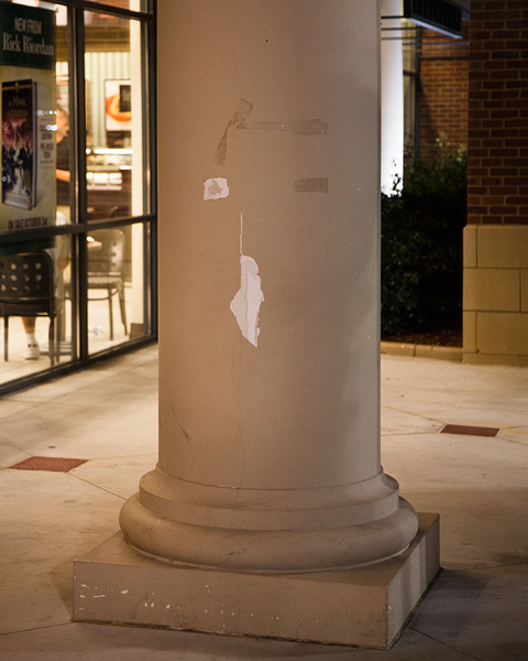 A smooth building column with some tape and scratch marks on it that look a little like an abstract face