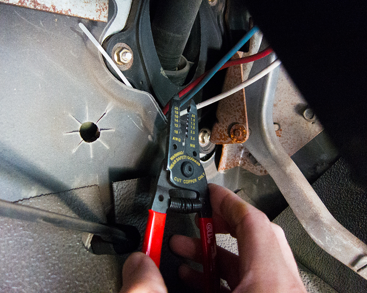 A photo of a pair of wirecutters about to cut a blue wire that's bundled with a red one and a white one going into the inside panel of a car doors inner mechanisms 